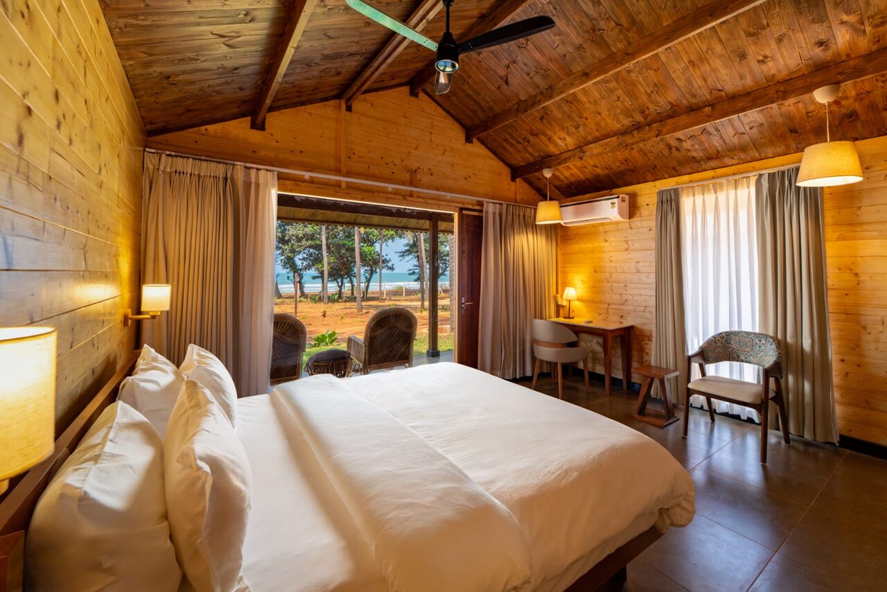 Wooden cottage bedroom with ocean view through open doors at Miraya by the Beach